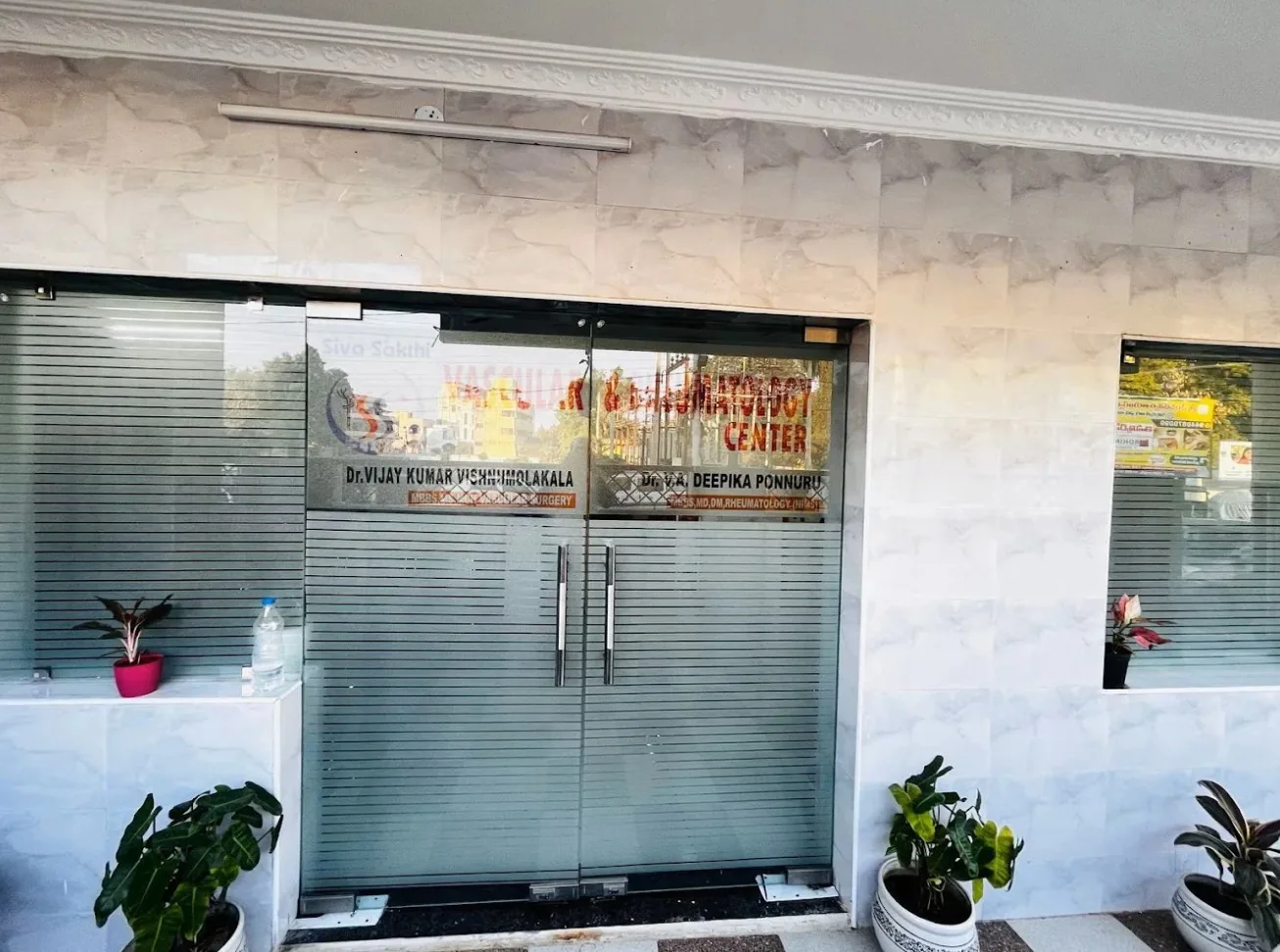 Glass entrance doors of Siva Sakthi Vascular & Rheumatology Center, Guntur, lettered with the names of Dr. Vijay Kumar Vishnumolakala and Dr. Deepika Ponnuru